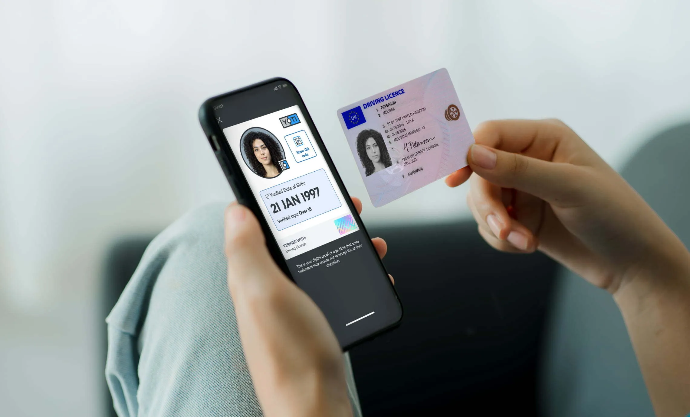 An image of a person holding smart phone in their left hand. On the phone's display is a Yoti Digital ID showing their verified credentials. In the person's right hand is their physical UK driving licence. The person is holding the two forms of ID next to each other.