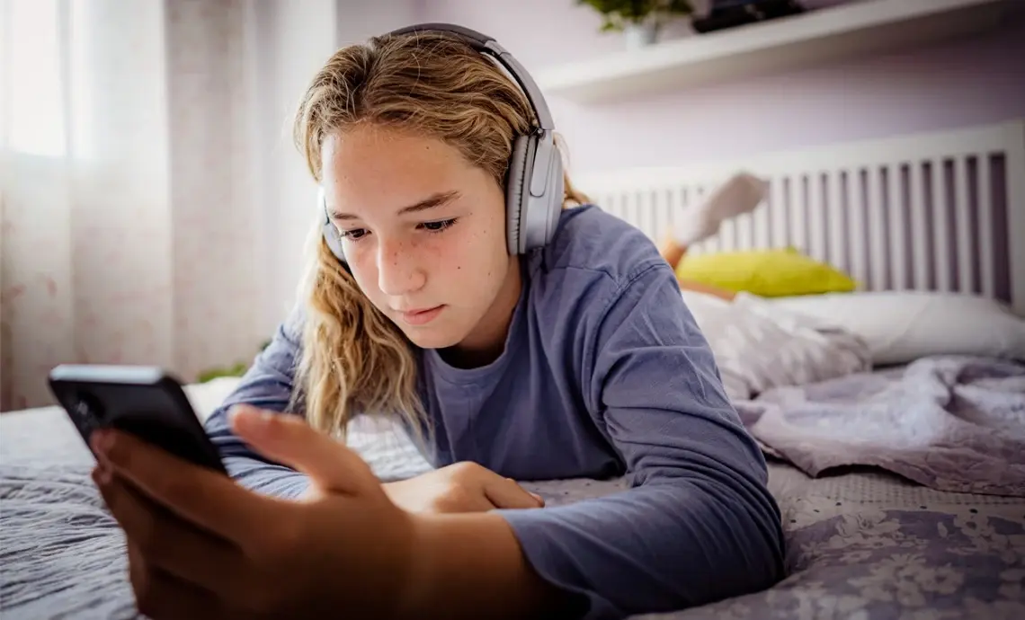 An image of a young person wearing a set of headphones and using their smartphone