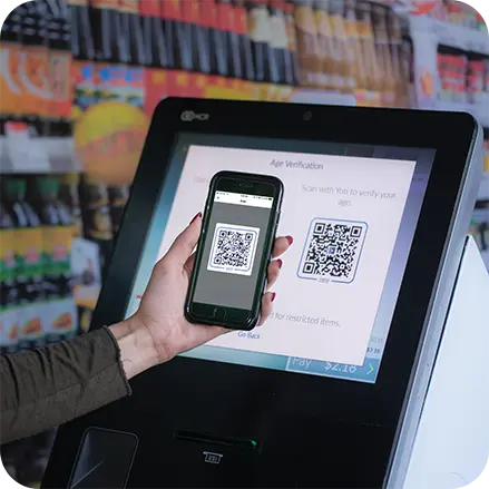 Person scanning age verification QR code on their phone at a supermarket self-checkout terminal