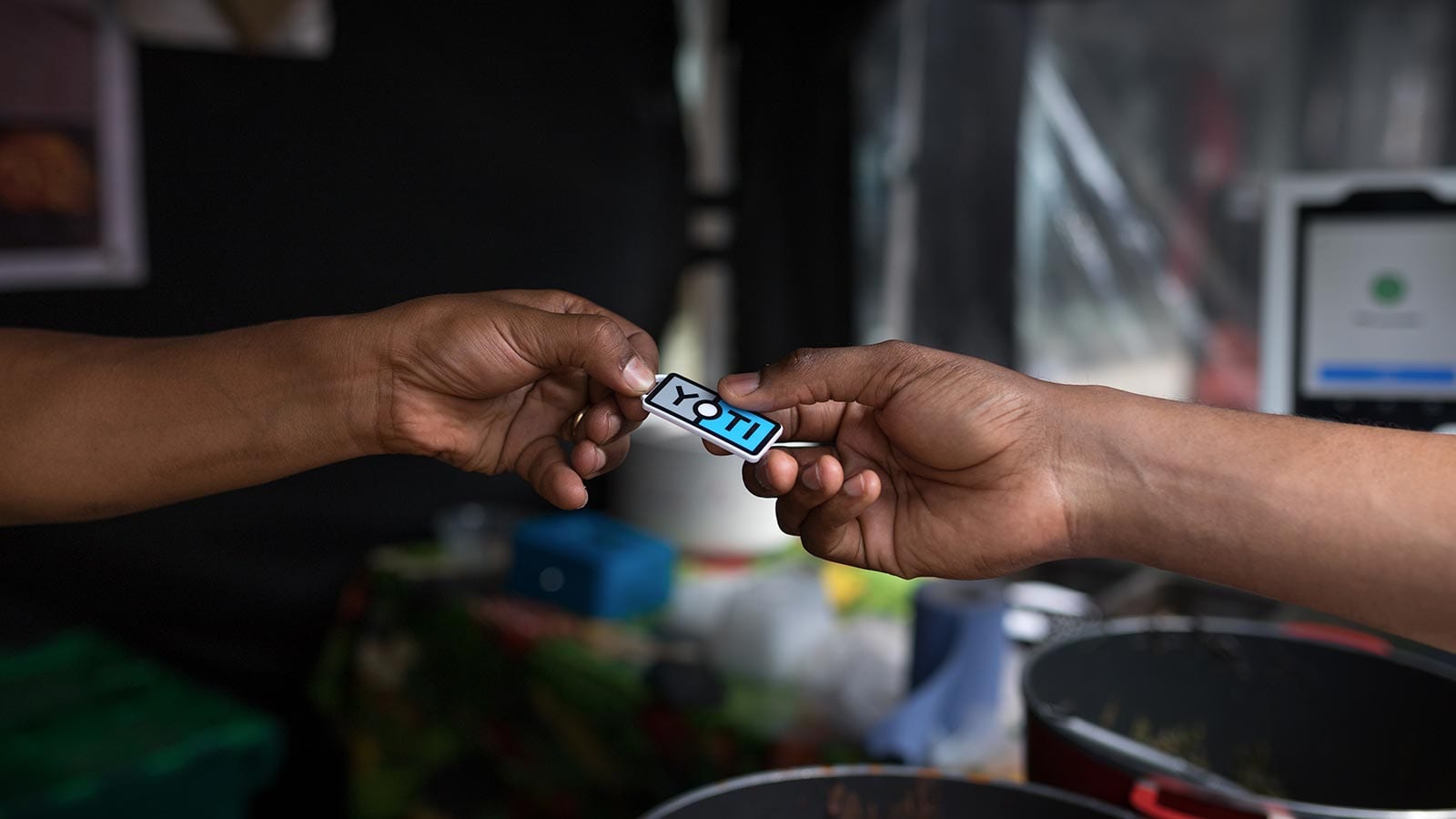 An image of two people's hands. One is handing a plastic tag, known as a Yoti Key, to the other.