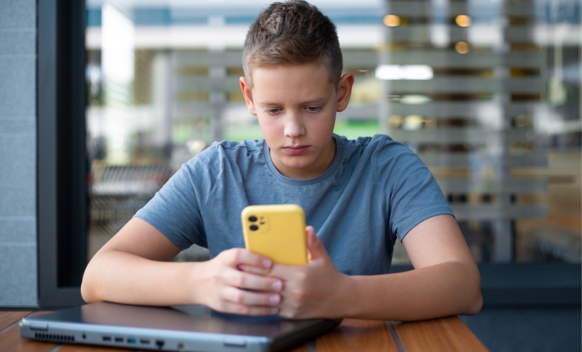 Teenage boy sat at desk using smartphone