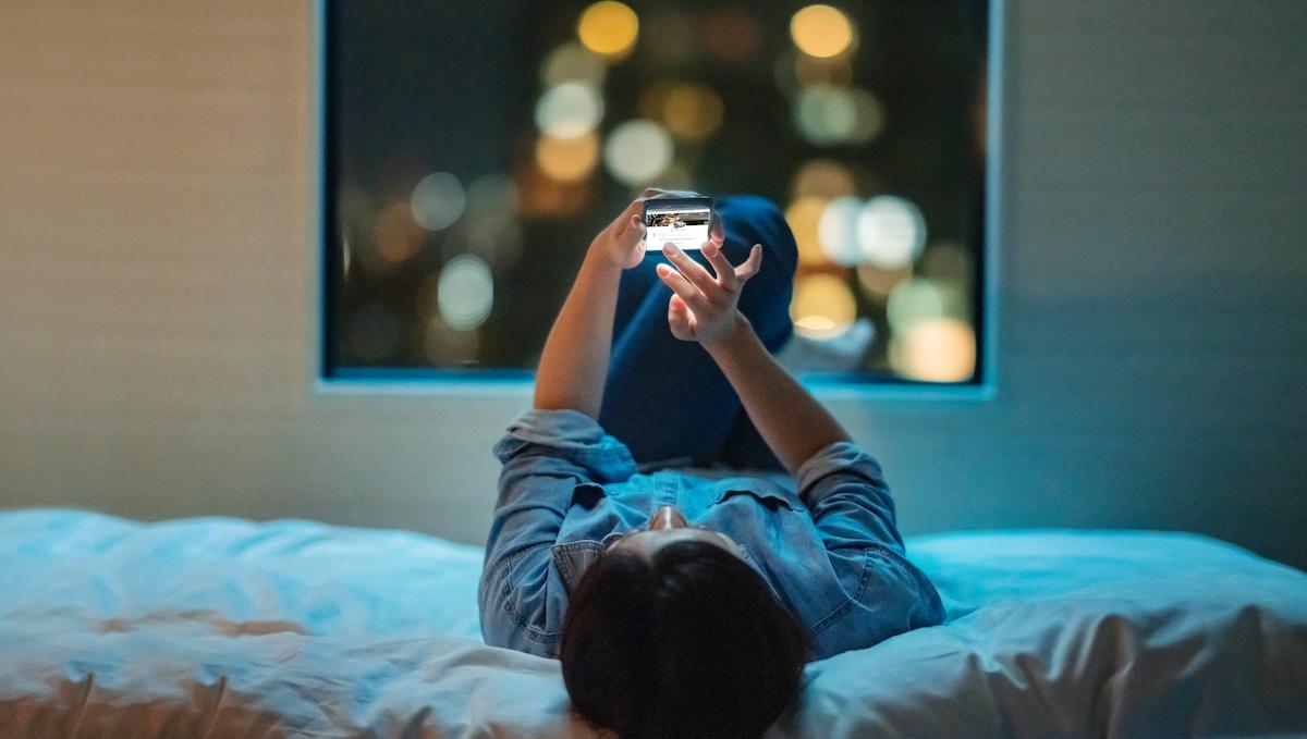 User laying on bed looking at smartphone