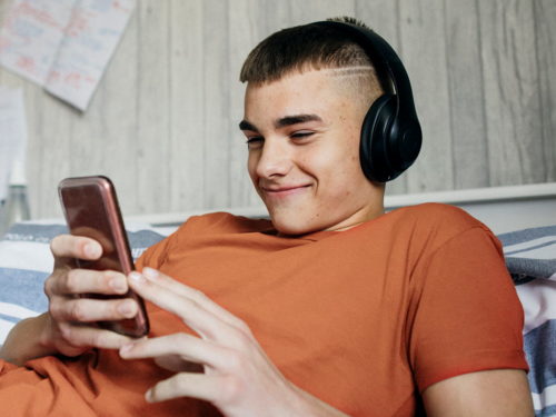 teenage boy lounging whilst looking at his phone and wearing over-ear headphones