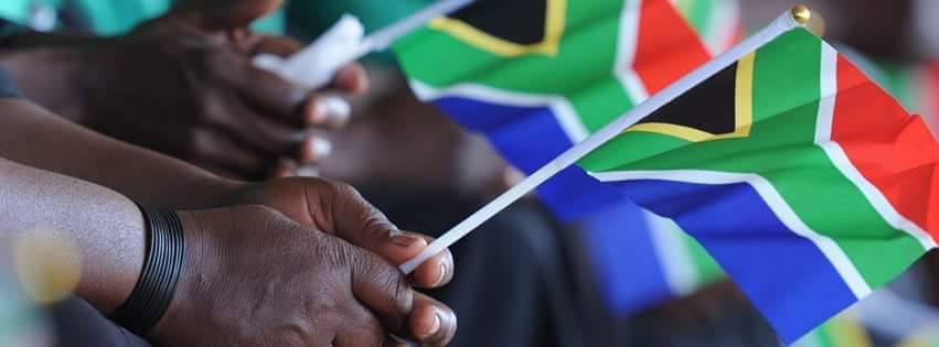 an image of two people's hands, each holding a small flag of South Africa