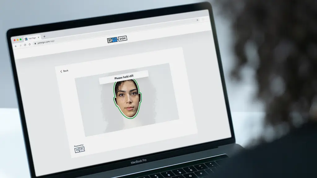 Laptop showing a woman's face on screen to perform face authentication within the Yoti Sign platform