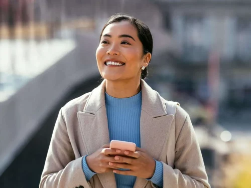 Smiling woman walking through city whilst using smartphone